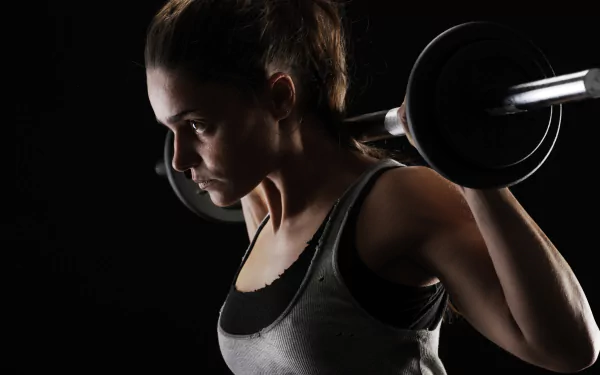 A brunette woman with brown eyes lifts a barbell, captured in sharp detail against a dark background in this 4K Ultra HD sports-themed wallpaper.