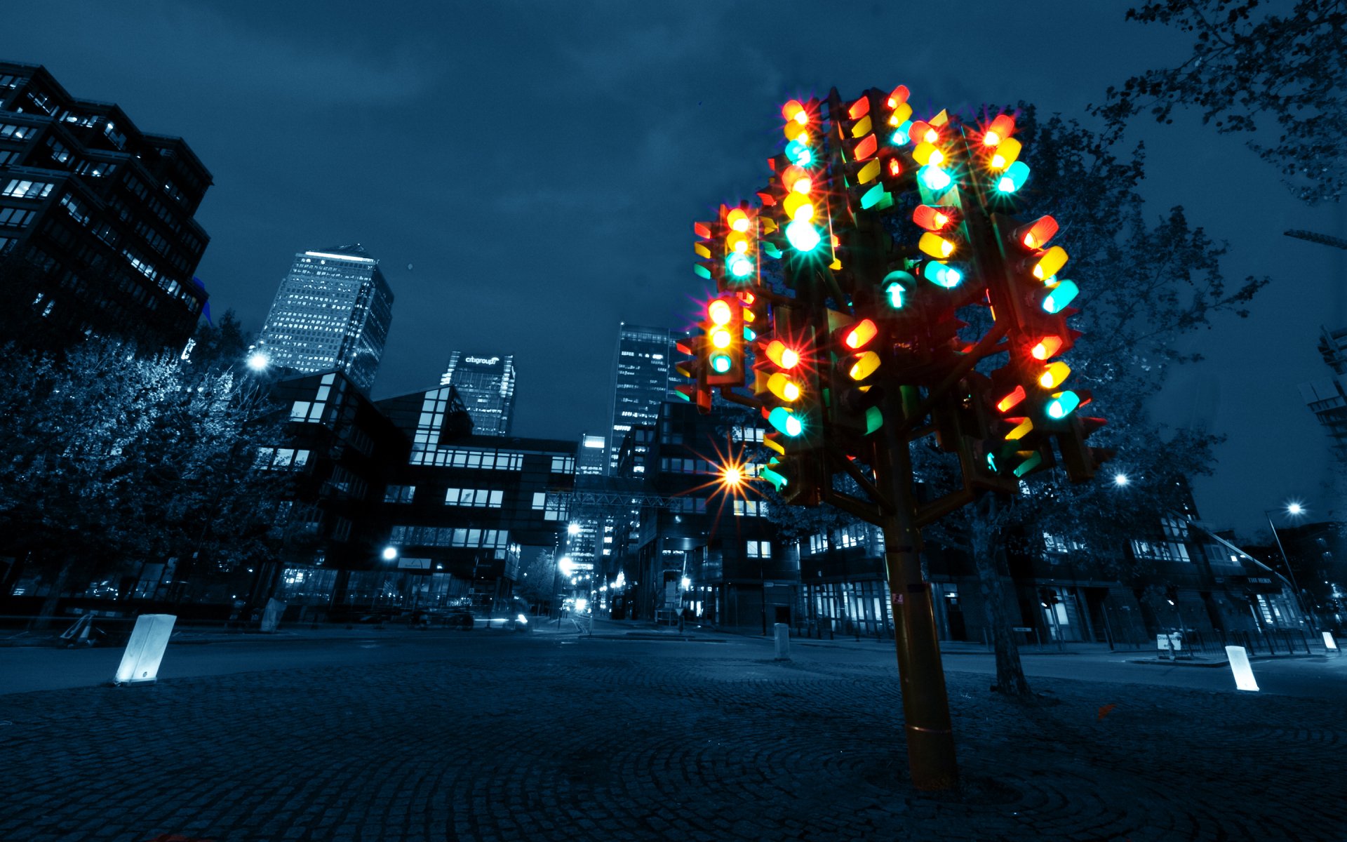 Vibrant multi-light traffic signal sculpture against a nighttime London cityscape — man-made art in England, 2K Quad HD PC desktop wallpaper and background.