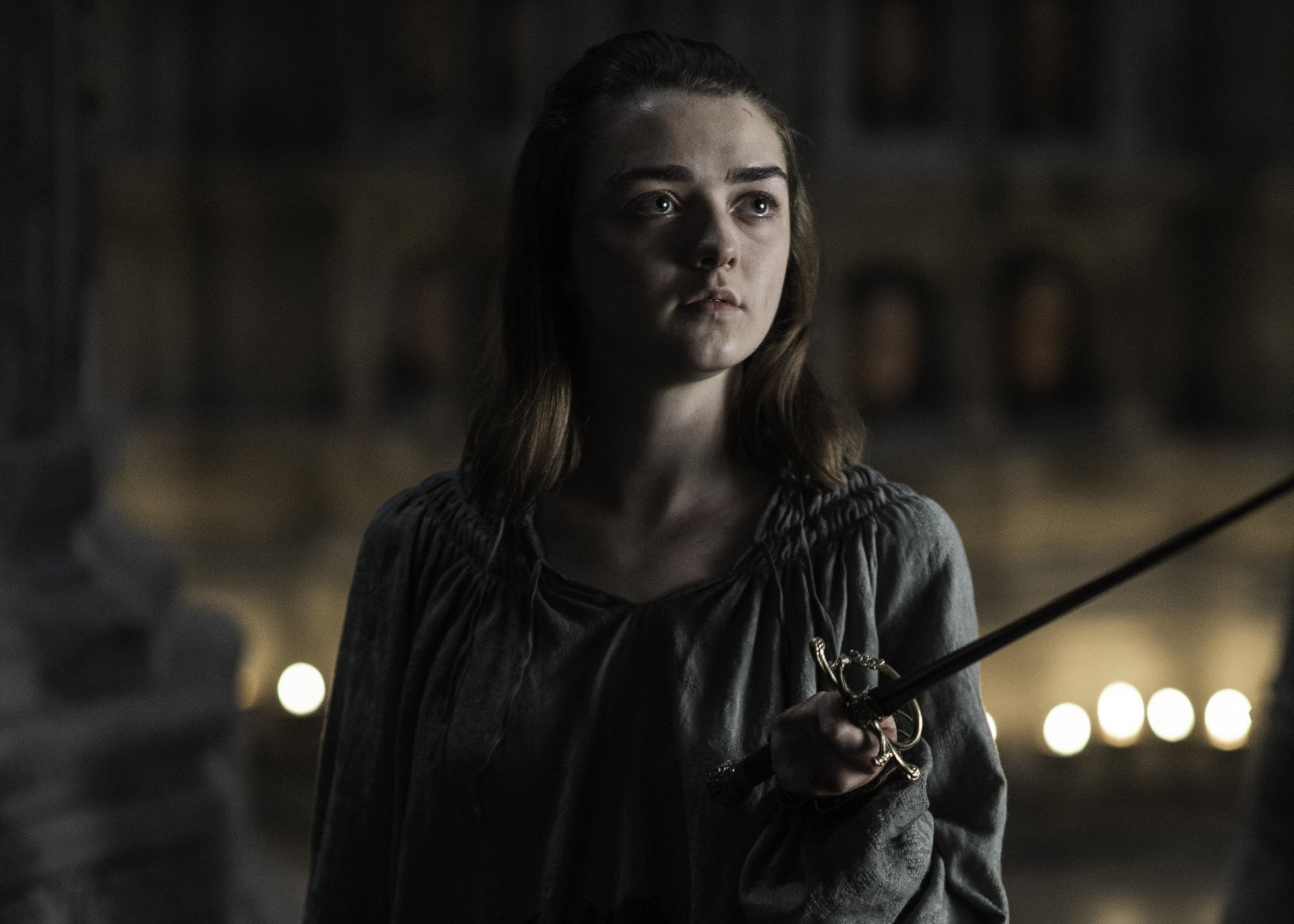 A high-definition wallpaper featuring Maisie Williams as Arya Stark from the TV show Game of Thrones, showcasing a determined expression with a sword in hand.