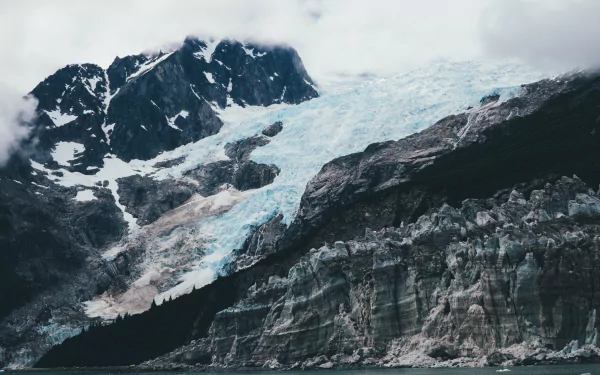 Snow-covered mountain with a glacier under a cloudy sky, captured in stunning 4K Ultra HD as a nature desktop wallpaper background.