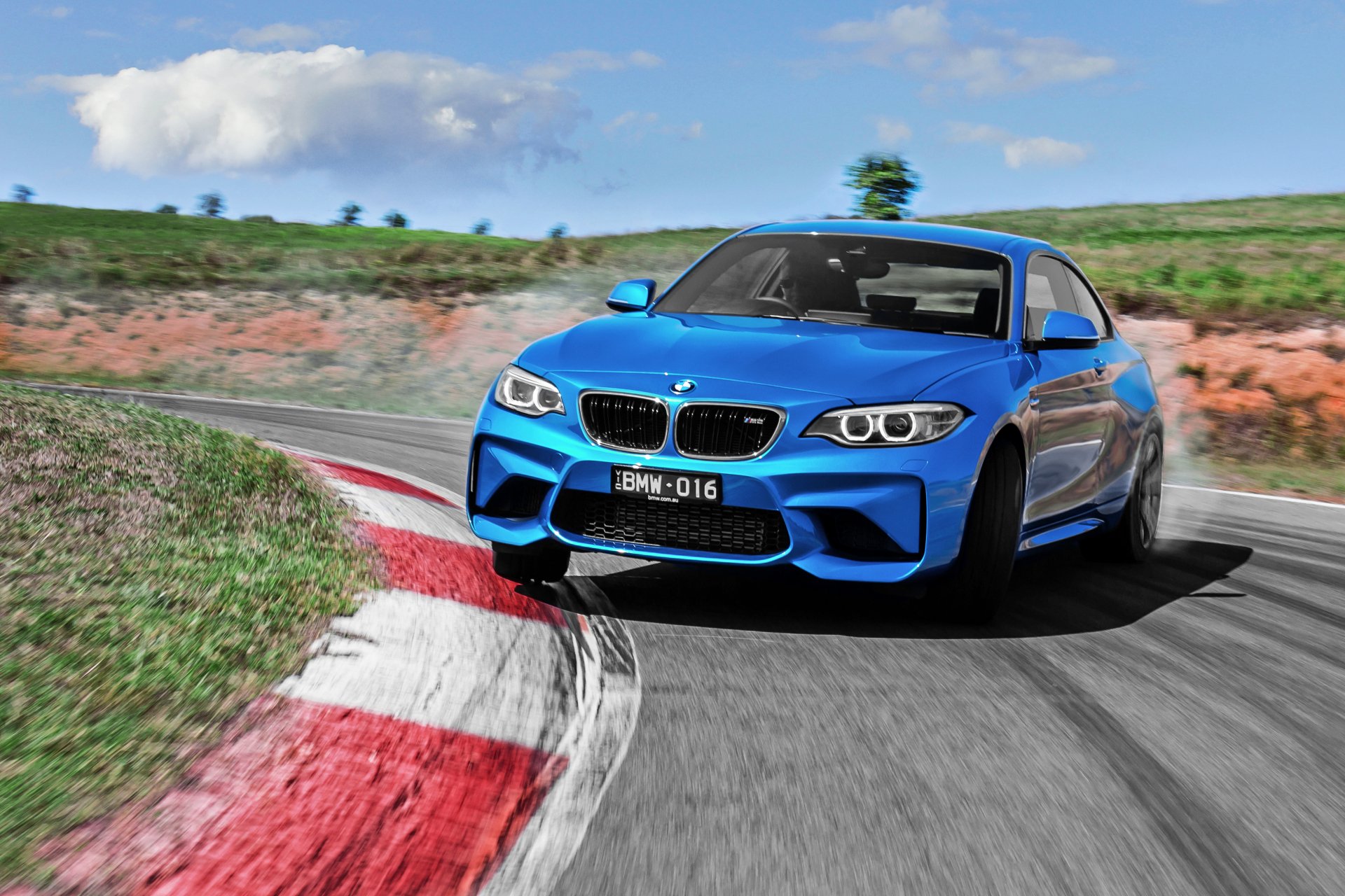 A vibrant blue BMW M2 car speeding on a racetrack with clear skies, captured as an HD PC desktop wallpaper showcasing the vehicle's dynamic design and performance.