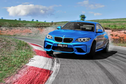 A vibrant blue BMW M2 car speeding on a racetrack with clear skies, captured as an HD PC desktop wallpaper showcasing the vehicle's dynamic design and performance.