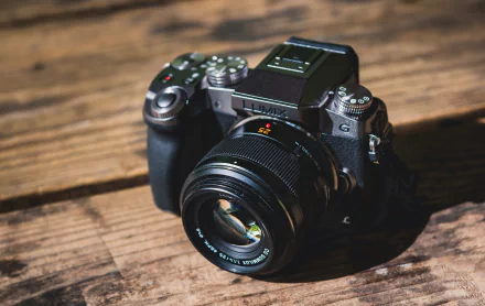 HD desktop wallpaper featuring a Lumix man-made camera placed on a wooden surface, showcasing detailed lens and body design in natural light.
