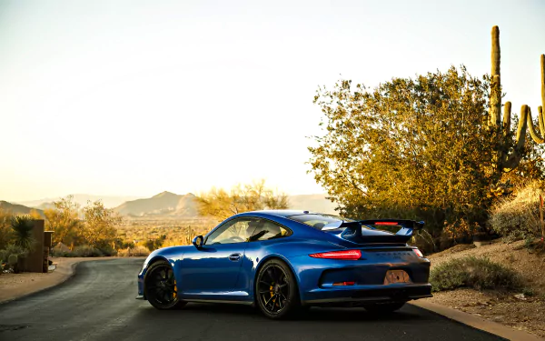 A blue Porsche 911 GT3 sports car parked on a desert road, surrounded by cacti and trees, showcased in a 4K Ultra HD wallpaper background.