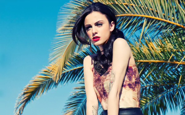 Brunette singer Cher Lloyd poses stylishly against a vibrant blue sky and palm backdrop, showcasing her bold red lipstick in this striking HD desktop wallpaper.