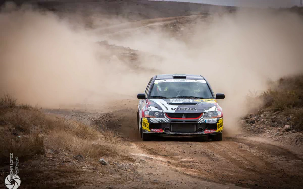 A Mitsubishi Lancer Evolution maneuvers through a dusty landscape, showcasing its rally-inspired design in this high-definition desktop wallpaper.