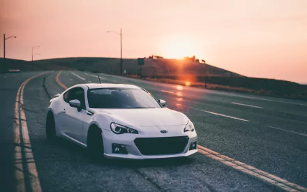 A white Subaru BRZ parked on a winding road during sunset, showcasing its sleek design against a vibrant sky, capturing a serene moment in an HD desktop wallpaper.