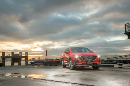 Red Mazda CX-9 SUV on a wet harbor pier beneath dramatic clouds at sunrise — 4K Ultra HD PC desktop wallpaper featuring the Mazda car and vehicle.