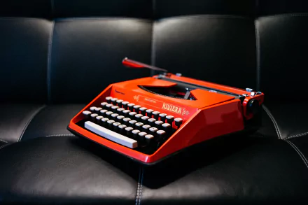 A vibrant red vintage typewriter resting on a black leather surface, captured in sharp detail as a 4K Ultra HD man-made PC desktop wallpaper.