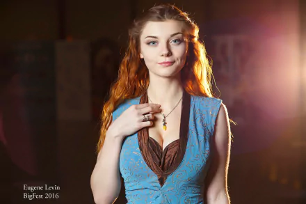 A woman in Margaery Tyrell cosplay from Game of Thrones, featuring vibrant red hair and an elegant blue dress, poses confidently against a softly lit background.