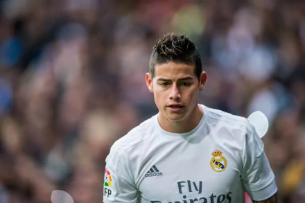HD desktop wallpaper featuring James Rodriguez in a Real Madrid C.F. jersey during a game. The blurred crowd in the background adds to the dynamic energy of the sports scene.