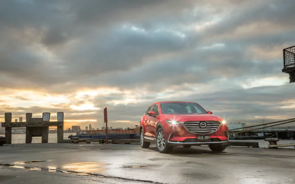 Red Mazda CX-9 SUV on a wet harbor pier beneath dramatic clouds at sunrise — 4K Ultra HD PC desktop wallpaper featuring the Mazda car and vehicle.