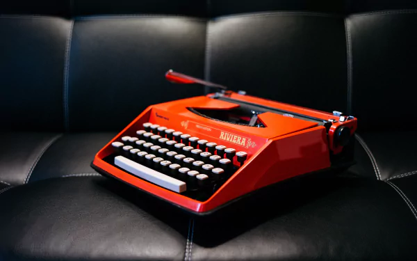 A vibrant red vintage typewriter resting on a black leather surface, captured in sharp detail as a 4K Ultra HD man-made PC desktop wallpaper.