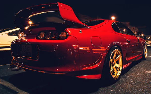 A vibrant red Toyota Supra parked at night, showcasing its sleek design and gold wheels, serves as an eye-catching HD desktop wallpaper and background.