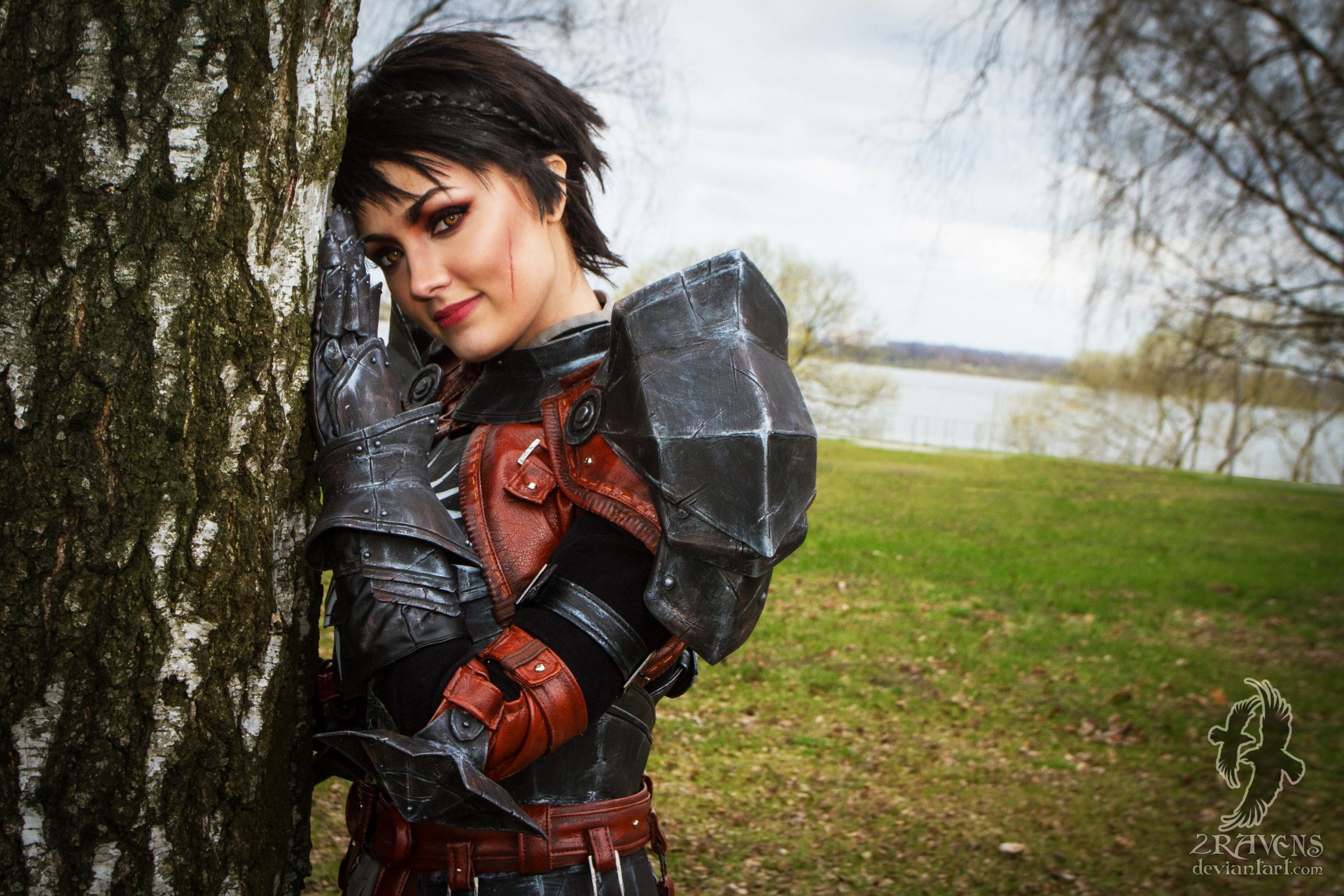 Brunette woman in detailed Cassandra Pentaghast cosplay from Dragon Age, posed against a tree in an outdoor setting, captured in 4K Ultra HD quality.