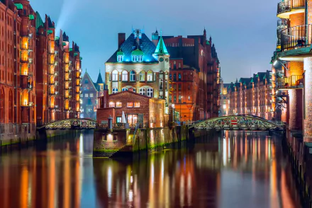 A stunning night view of Hamburg's canals, showcasing beautifully illuminated buildings and a charming structure with a teal-roofed tower reflecting on the water. Man-made beauty in Germany.
