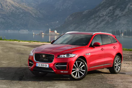 Red Jaguar F-PACE SUV parked by a lake with mountains in the background, captured in a high-definition desktop wallpaper showcasing the luxury vehicle.