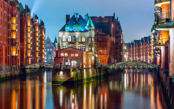 A stunning night view of Hamburg's canals, showcasing beautifully illuminated buildings and a charming structure with a teal-roofed tower reflecting on the water. Man-made beauty in Germany.