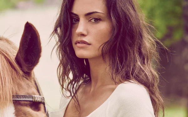 Brunette woman with wavy hair gazing at the camera beside a horse in soft outdoor light; 2K Quad HD PC desktop wallpaper/background.