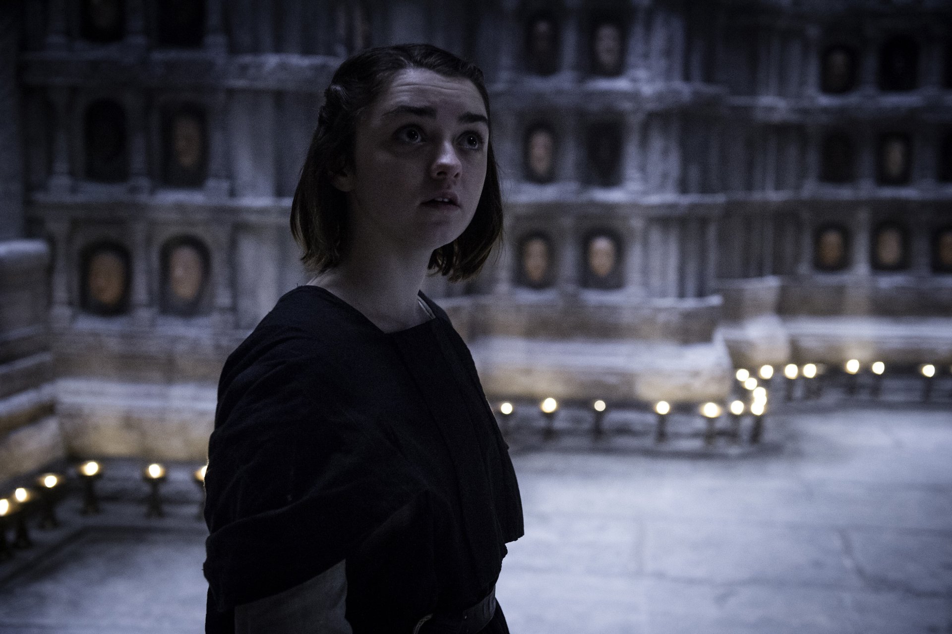 Maisie Williams as Arya Stark from Game of Thrones stands thoughtfully in a dimly lit chamber, captured in 4K Ultra HD for a PC desktop wallpaper.