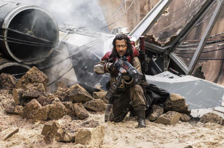 Jiang Wen as Saw Gerrera in Rogue One: A Star Wars Story, poised with a blaster amidst rubble and smoke, embodies the intense action of this iconic sci-fi film. 4K Ultra HD wallpaper.