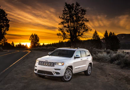 White Jeep Grand Cherokee SUV parked near a road at sunrise, set against a vibrant orange sky and silhouetted trees, captured as an HD desktop wallpaper background.