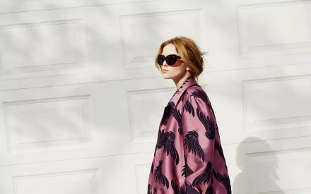Brunette woman in sunglasses and a pink patterned coat poses before a white garage door — HD PC desktop wallpaper background.