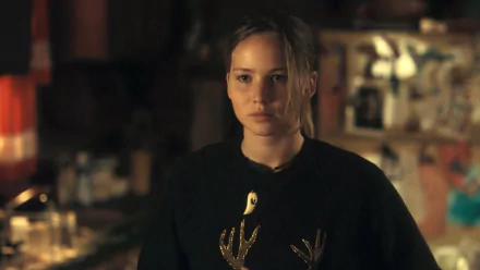 HD PC wallpaper — still from Winter's Bone: a young woman with a solemn gaze in a dim, cluttered interior, wearing a dark sweater with a gold antler design.
