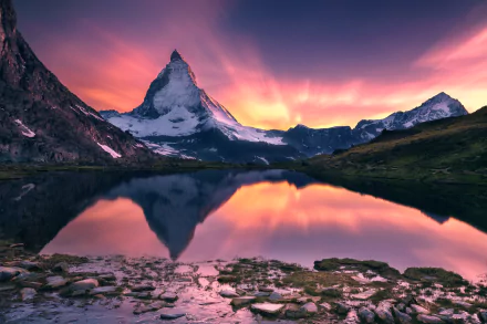 A stunning sunset over the Alps reflects beautifully in a tranquil lake, showcasing the majestic Matterhorn and surrounding mountains in vibrant colors.