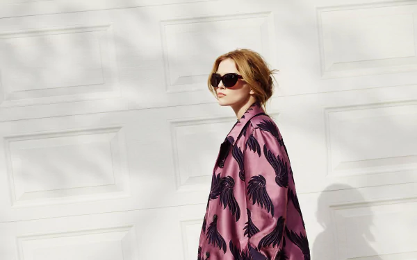 Brunette woman in sunglasses and a pink patterned coat poses before a white garage door — HD PC desktop wallpaper background.