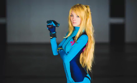A woman cosplays as Samus Aran from Metroid, showcasing a detailed blue and black suit. The image serves as a striking HD desktop wallpaper and background.