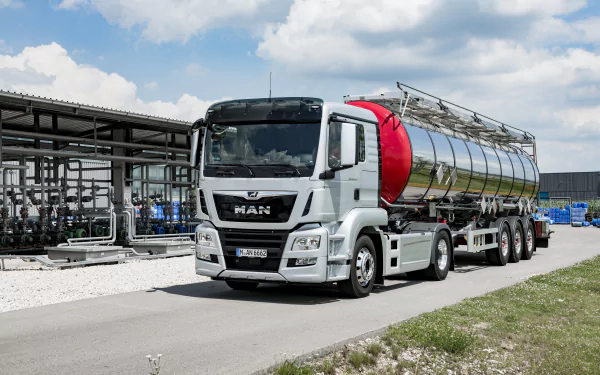 4K Ultra HD desktop wallpaper of a man driving a large MAN tanker truck on an industrial road under a partly cloudy sky.