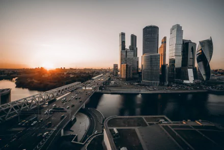 A stunning Moscow cityscape at sunrise, featuring towering skyscrapers along a bustling highway bordered by a serene river, showcasing the vibrant energy of this man-made landscape.