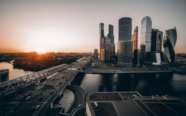 A stunning Moscow cityscape at sunrise, featuring towering skyscrapers along a bustling highway bordered by a serene river, showcasing the vibrant energy of this man-made landscape.