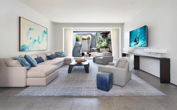 A modern living room featuring a spacious sofa, a stylish coffee table, and a large television, with natural light pouring in from an open area, creating a welcoming atmosphere.
