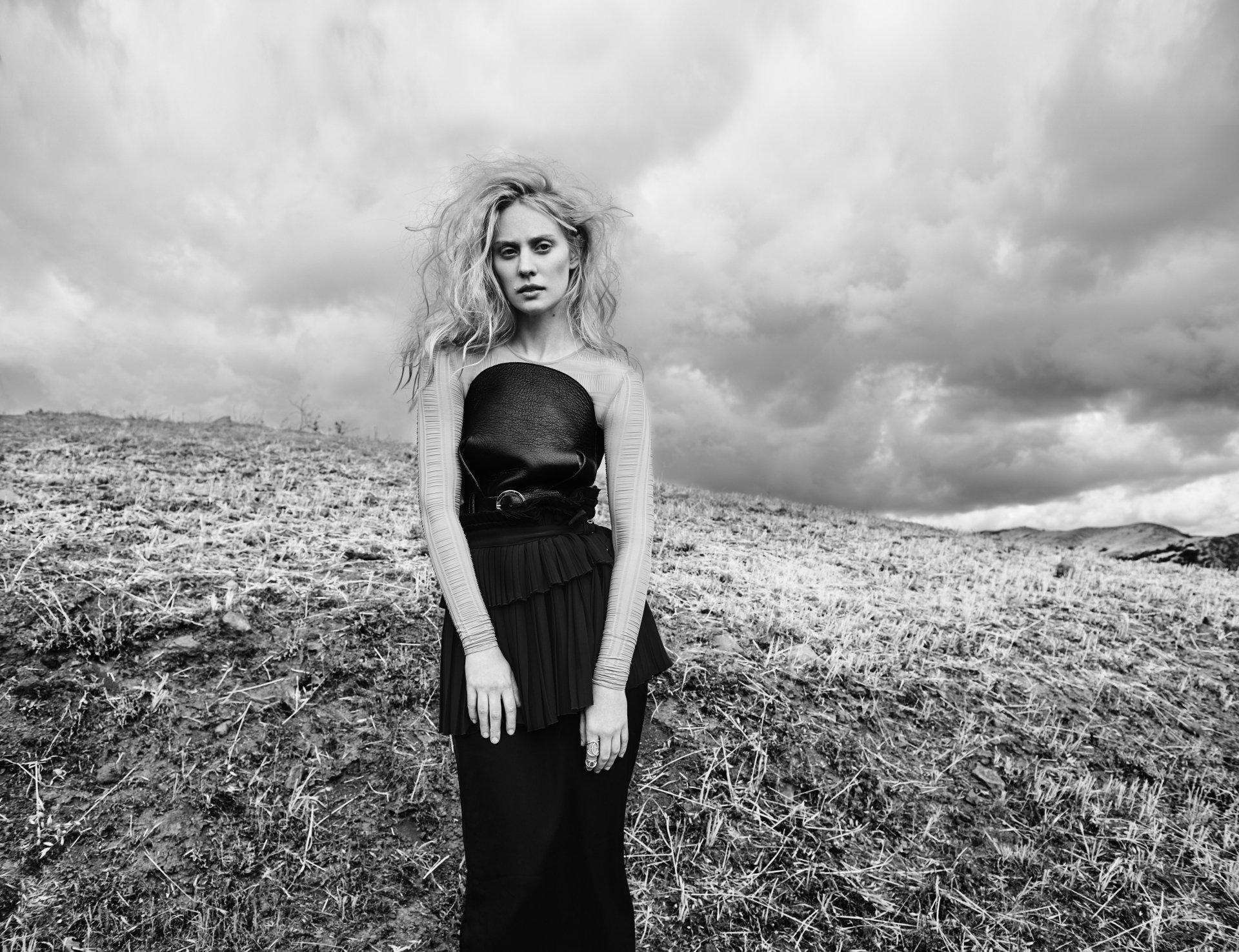 Black & White 5K Ultra HD PC desktop wallpaper: outdoor woman model stands on a windswept hillside under dramatic clouds in a strapless black dress.