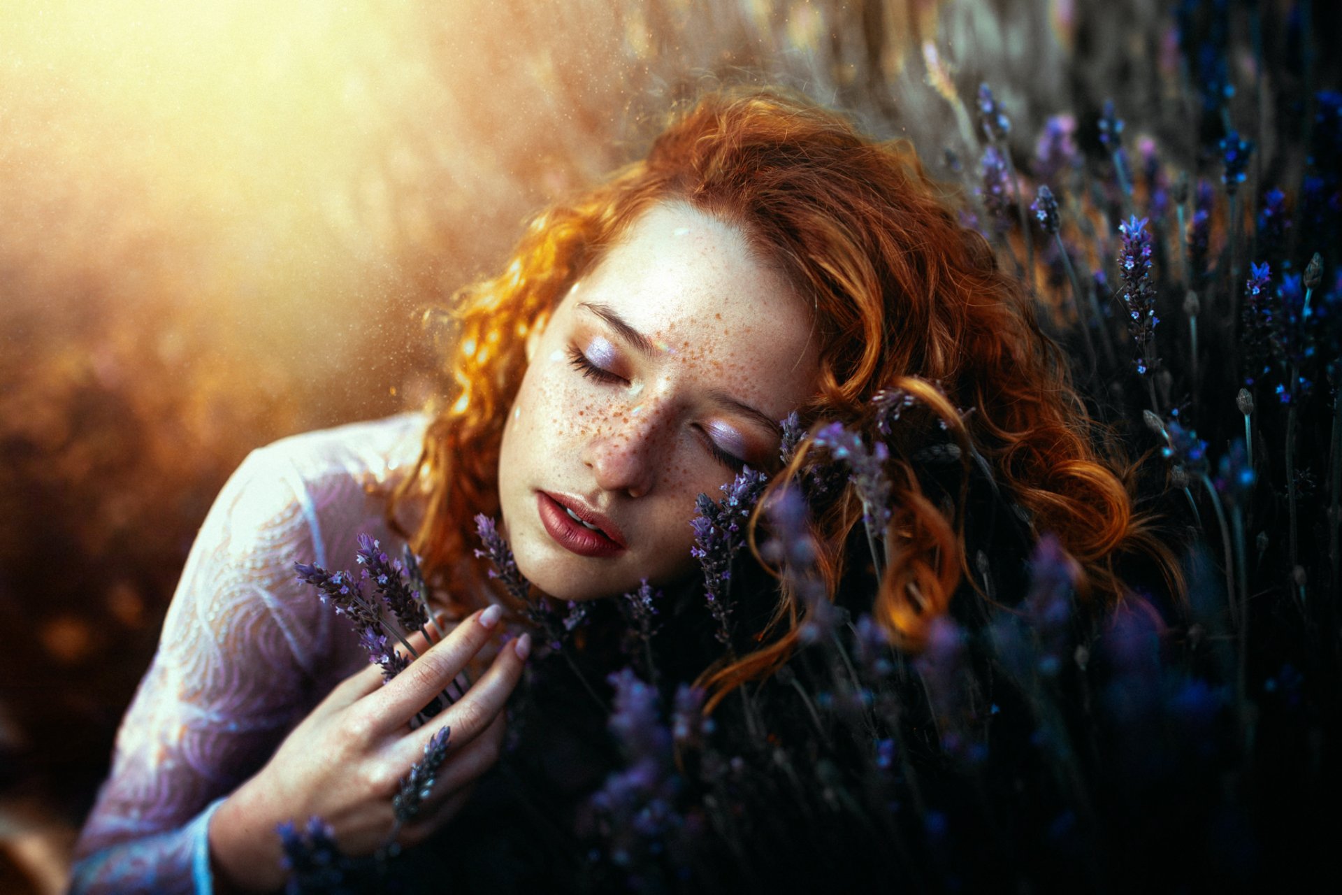 HD desktop wallpaper of a redhead woman with freckles and lipstick, lying down in a sunny field of lavender, her serene face softly illuminated.