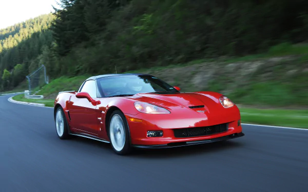 Red Chevrolet Corvette (C6) sports car speeding along a tree-lined road, rendered as a 2K Quad HD PC desktop wallpaper/background.