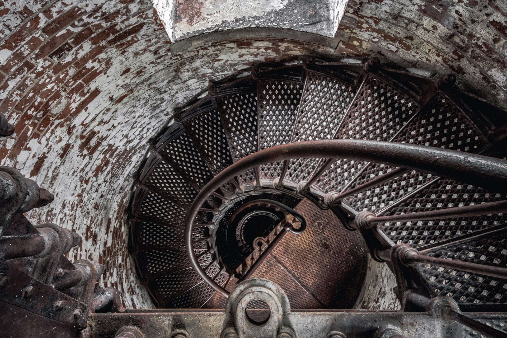 A high-definition desktop wallpaper showing a man-made spiral staircase with textured metal steps and aged, weathered walls surrounding it.