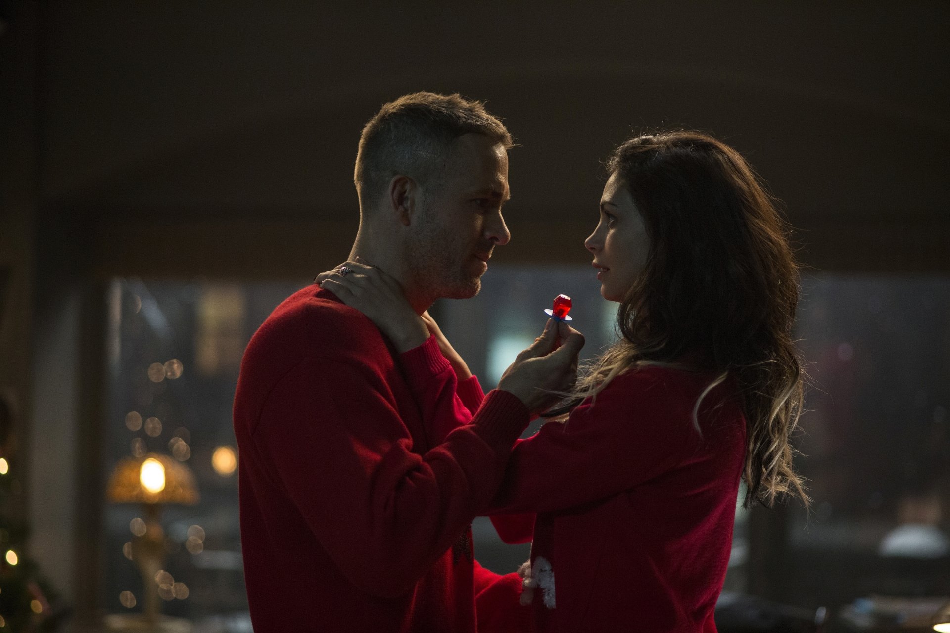 Morena Baccarin and Ryan Reynolds share a romantic moment in this HD wallpaper from the movie Deadpool, capturing their chemistry against a warm, cozy backdrop.
