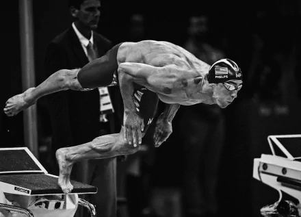 A competitive swimmer diving off the starting block, captured in a dynamic black and white style, showcasing the intensity of swimming sports as an HD desktop wallpaper.