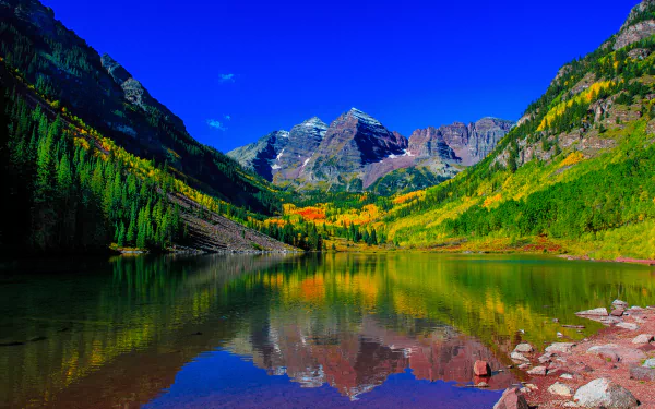 A vibrant 4K Ultra HD image of Maroon Lake in Colorado reflects lush forests and the iconic Rocky Mountains peaks under a clear blue sky.