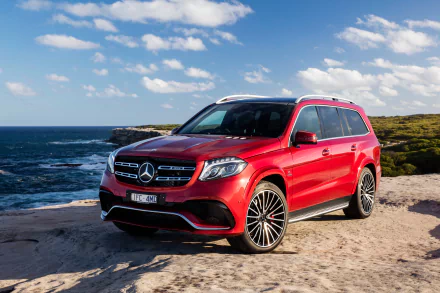 A red Mercedes-Benz GL-Class SUV parked on a rocky coastline under a blue sky, captured in 4K Ultra HD for a desktop wallpaper background.