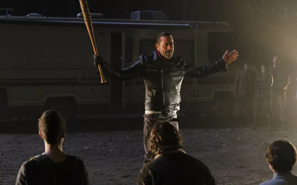 Jeffrey Dean Morgan as Negan from The Walking Dead stands confidently with a bat, addressing a group, set against a backdrop of an RV and a dark, eerie atmosphere.