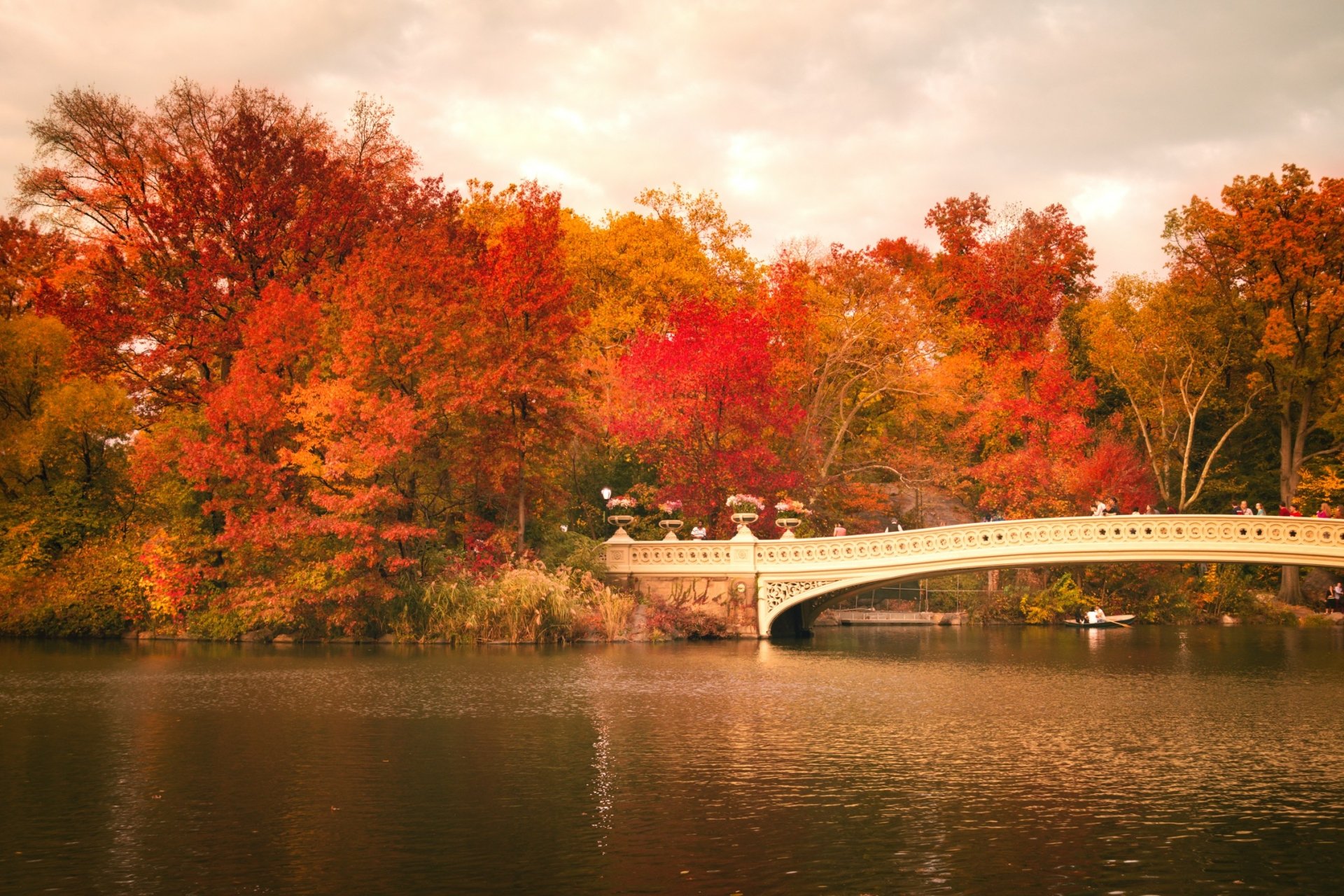 HD PC desktop wallpaper: Bow Bridge spanning a calm Central Park river amid vibrant fall foliage, man-made bridge reflected in the water.