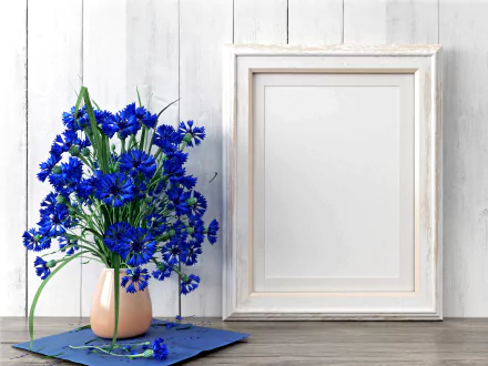 5K Ultra HD still life photography: vivid blue cornflower bouquet in a pale vase beside an empty white frame on rustic white boards — PC desktop wallpaper.