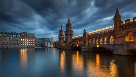 A stunning night view of a bridge in Berlin, Germany, reflecting in the river under a dramatic sky. The image showcases the city's man-made beauty in rich 4K Ultra HD detail.
