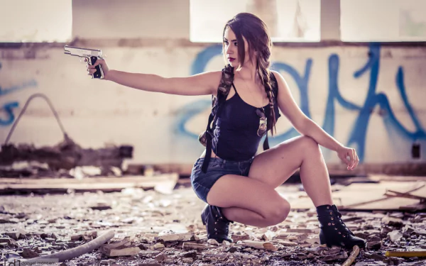 A confident woman crouches in an abandoned space, aiming a gun. She wears a black tank top and shorts, surrounded by urban decay, captured in a striking HD desktop wallpaper.