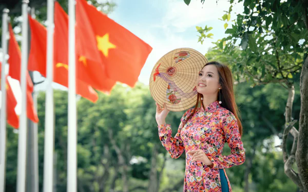 A smiling woman with brown eyes and brunette hair wears a traditional costume and hat, standing among flags, showcasing cultural beauty in a vibrant outdoor setting.