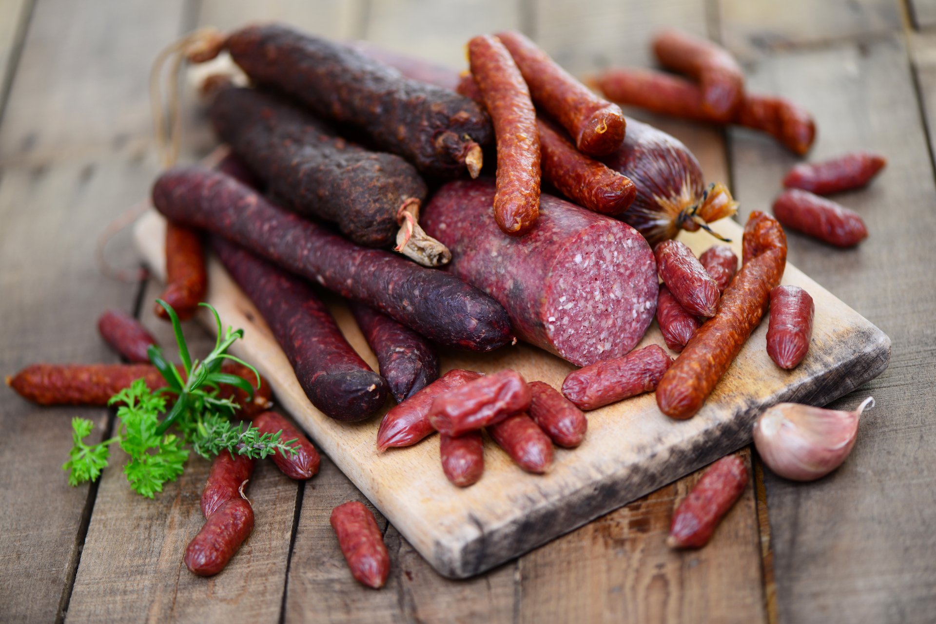 4K Ultra HD desktop wallpaper featuring an assortment of cured meats and sausages arranged on a wooden cutting board with fresh herbs and garlic.